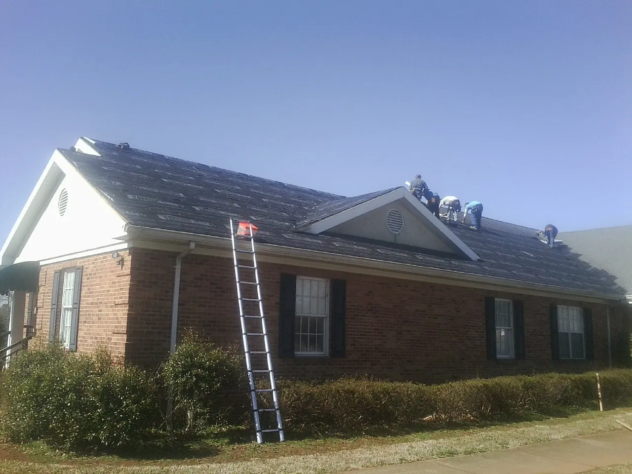 Crew tearing shingles off a brick ranch roof with a ladder set — Emergency Roof Repair work by our crew in Eddyville