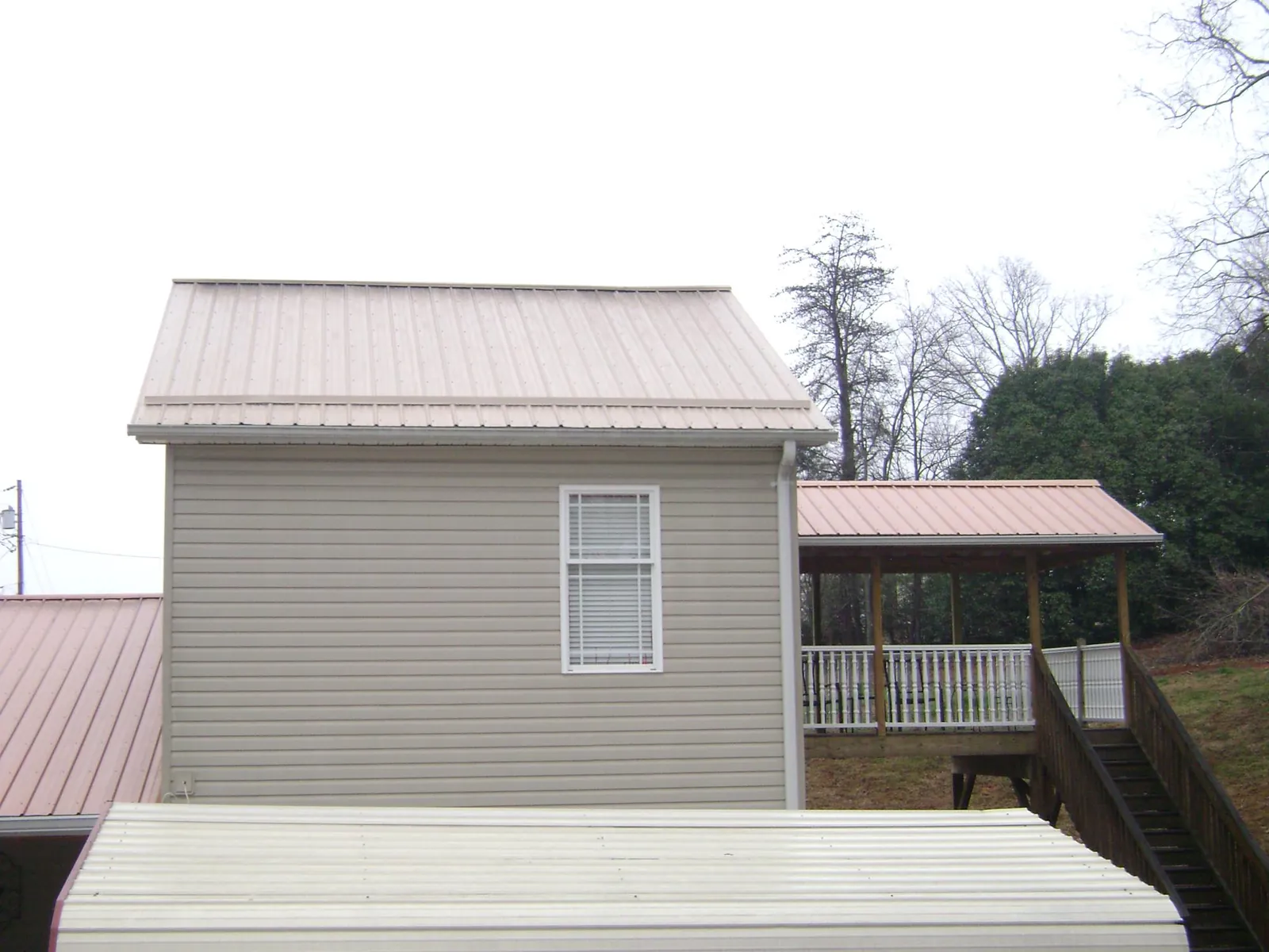 Tan metal roofs on a two story addition and attached porch, from a Roof Replacement job in Eddyville